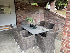 Uma área de pátio com mesa e cadeiras de vime, um muro de tijolos e uma árvore.