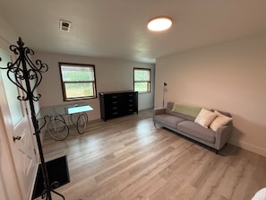 Una habitación con piso de madera, un sofá, un escritorio y dos ventanas con persianas.