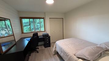 Ein Schlafzimmer mit Bett, Schreibtisch mit Stuhl, Fenster und Tür.