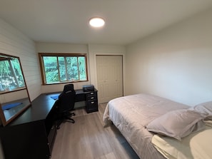 Un dormitorio con una cama, un escritorio con silla, una ventana y una puerta.