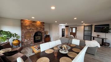 A dining area with a brick fireplace, a sofa, and a television mounted on the wall.