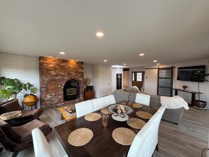 A dining area with a brick fireplace, a sofa, and a television mounted on the wall.