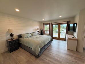 Quarto com cama, mesas de cabeceira, televisão e varanda com vista.