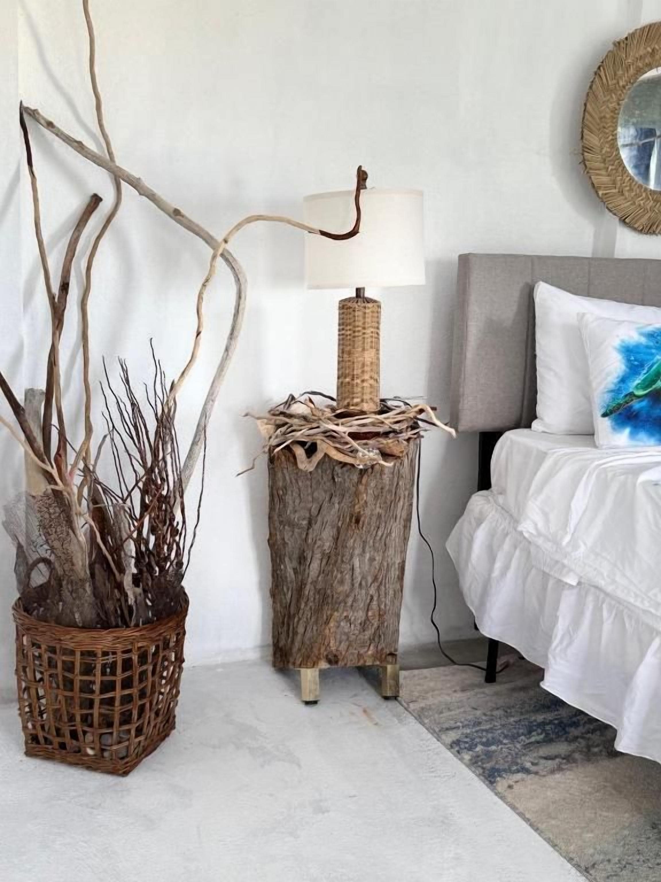 A bedroom with a bed, a bedside lamp, a wall-mounted mirror, and a decorative plant arrangement.