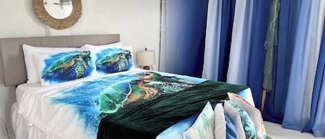 Una cama con diseño de tortuga marina, un espejo redondo y cortinas azules.