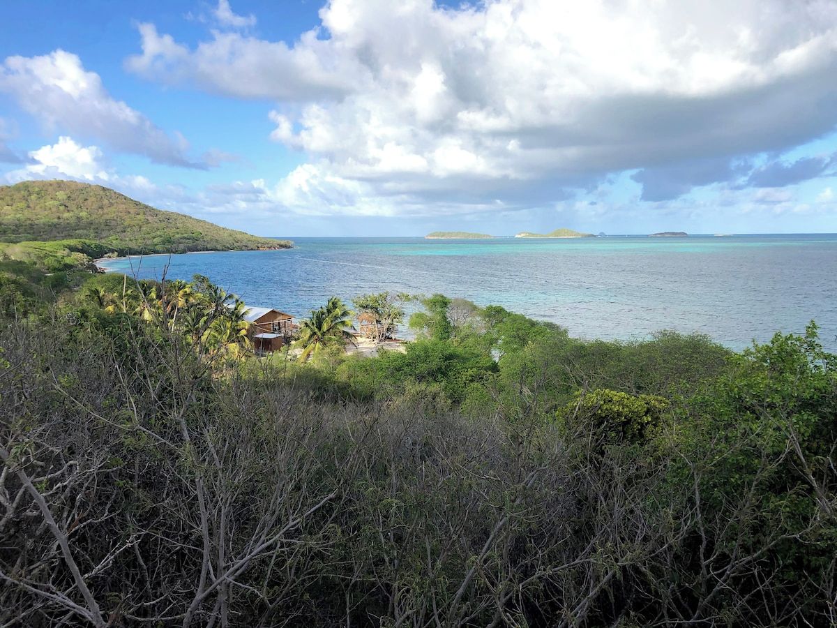 A coastal landscape with a view of the sea, a small cluster of buildings, and a hilly background.