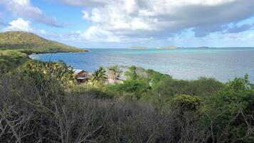 A coastal landscape with a view of the sea, a small cluster of buildings, and a hilly background.