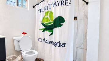 A bathroom with a shower curtain featuring a green turtle and the text 'it's down to together.'