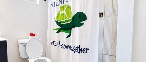 A bathroom with a shower curtain featuring a green turtle and the text 'it's down to together.'