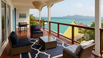 A balcony with wicker furniture, a table, and a view of the sea.