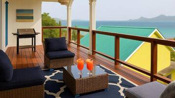 A balcony with wicker furniture, a table with drinks, and a view of the ocean.