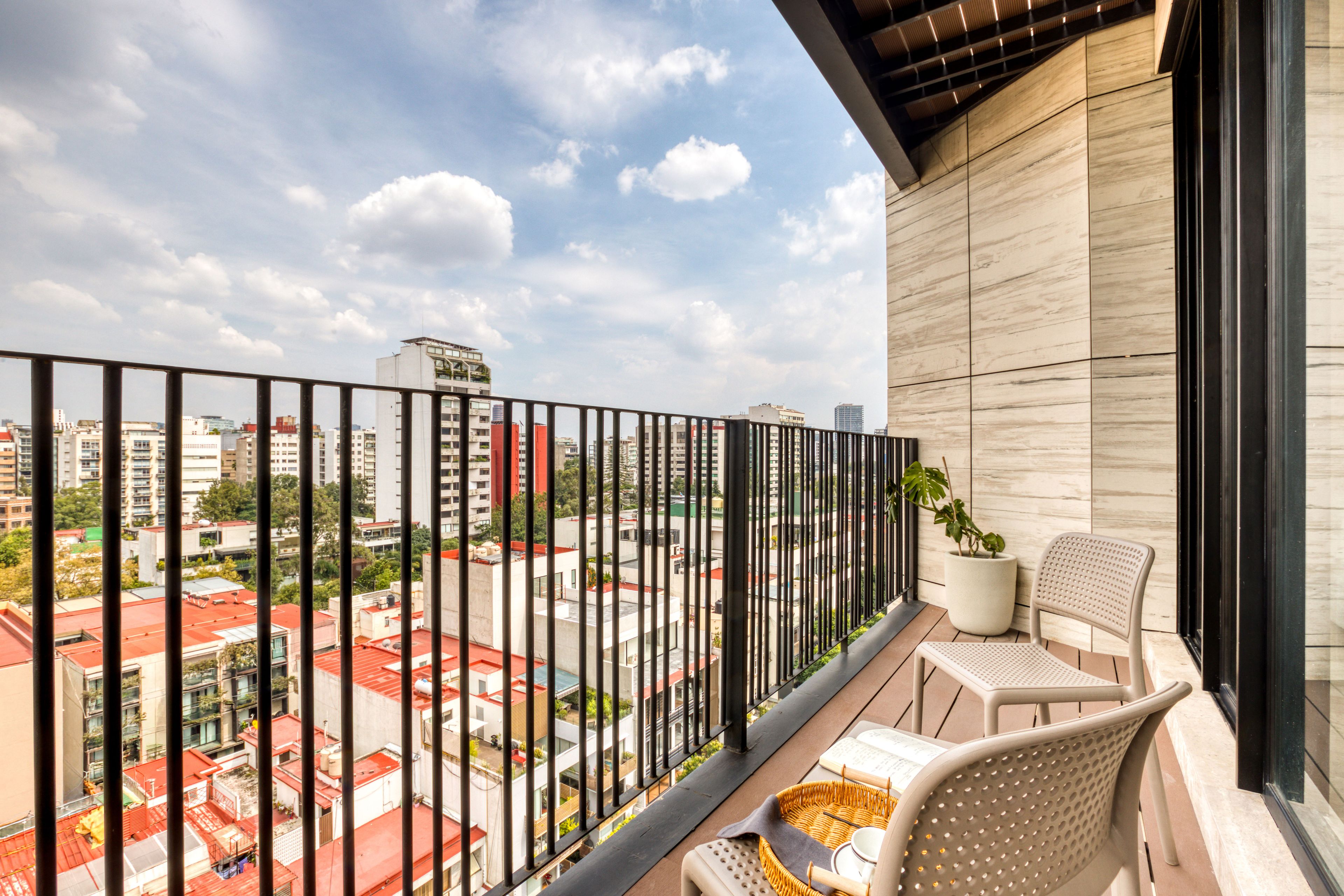 Un balcón con vistas a un paisaje urbano, una planta en maceta y un área de descanso con una silla y una mesa.