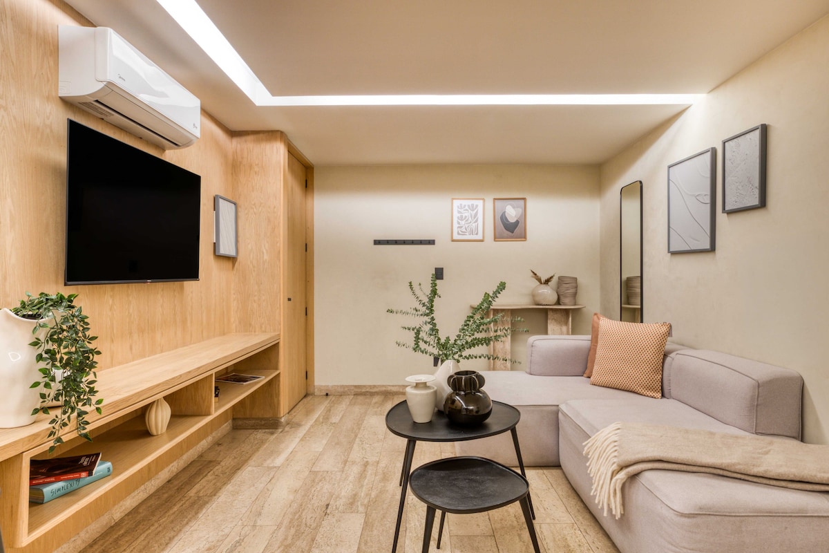 Uma sala de estar moderna com televisão de tela plana, unidade de entretenimento de madeira, sofá, mesa de centro e uma pequena mesa lateral com objetos decorativos.