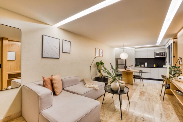 Una sala moderna con un sofá, una mesa de centro y una cocina al fondo.