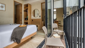 Habitación de hotel moderna con cama, banca, silla, espejo y vistas al exterior.