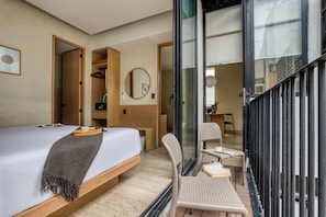 Quarto de hotel moderno com cama, um banco, uma cadeira, um espelho e vista para o exterior.
