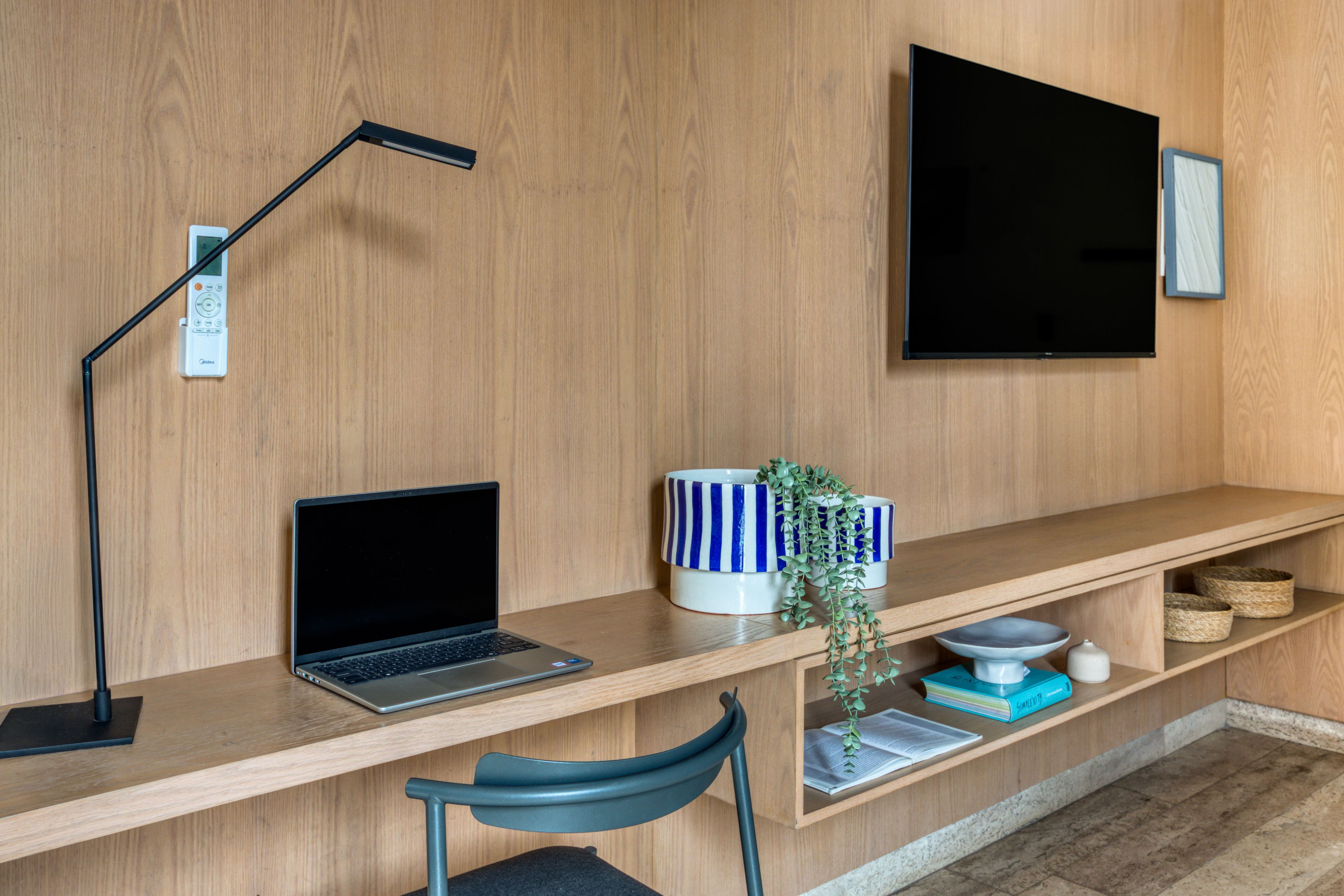 Un espacio de trabajo moderno con una laptop, una lámpara de escritorio, un televisor y una estantería con adornos.