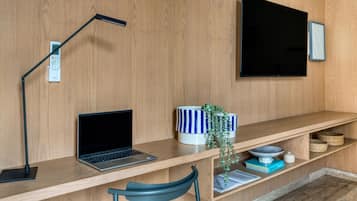 Un espacio de trabajo moderno con una laptop, una lámpara de escritorio, un televisor y una estantería con adornos.