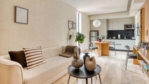 Una sala de estar moderna con un sofá, una mesa de centro con jarrones decorativos y vista al área de la cocina.