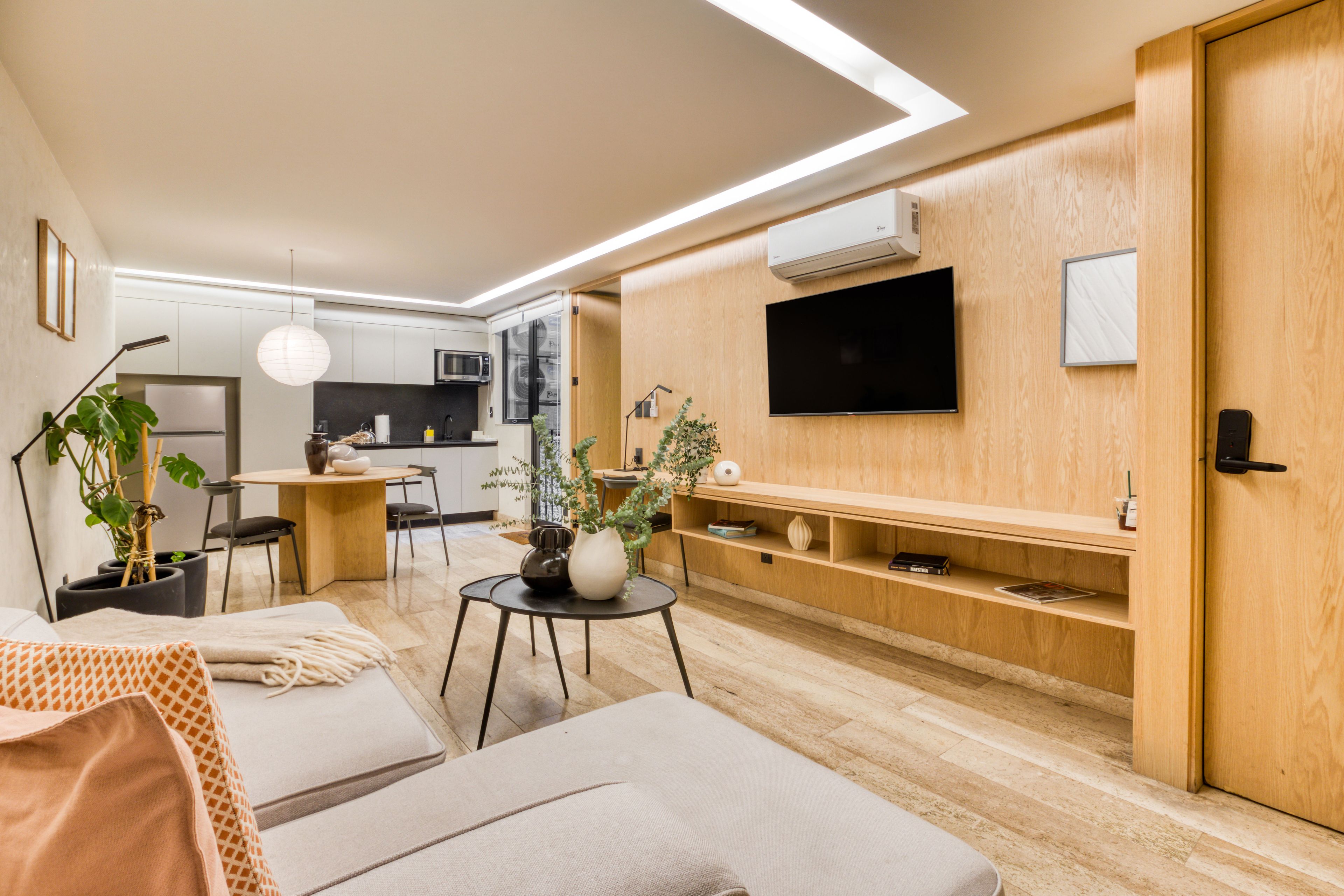 Una sala moderna con sofá, comedor con mesa y sillas, cocina equipada y televisor montado en la pared.