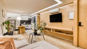 Una sala moderna con sofá, comedor con mesa y sillas, cocina equipada y televisor montado en la pared.