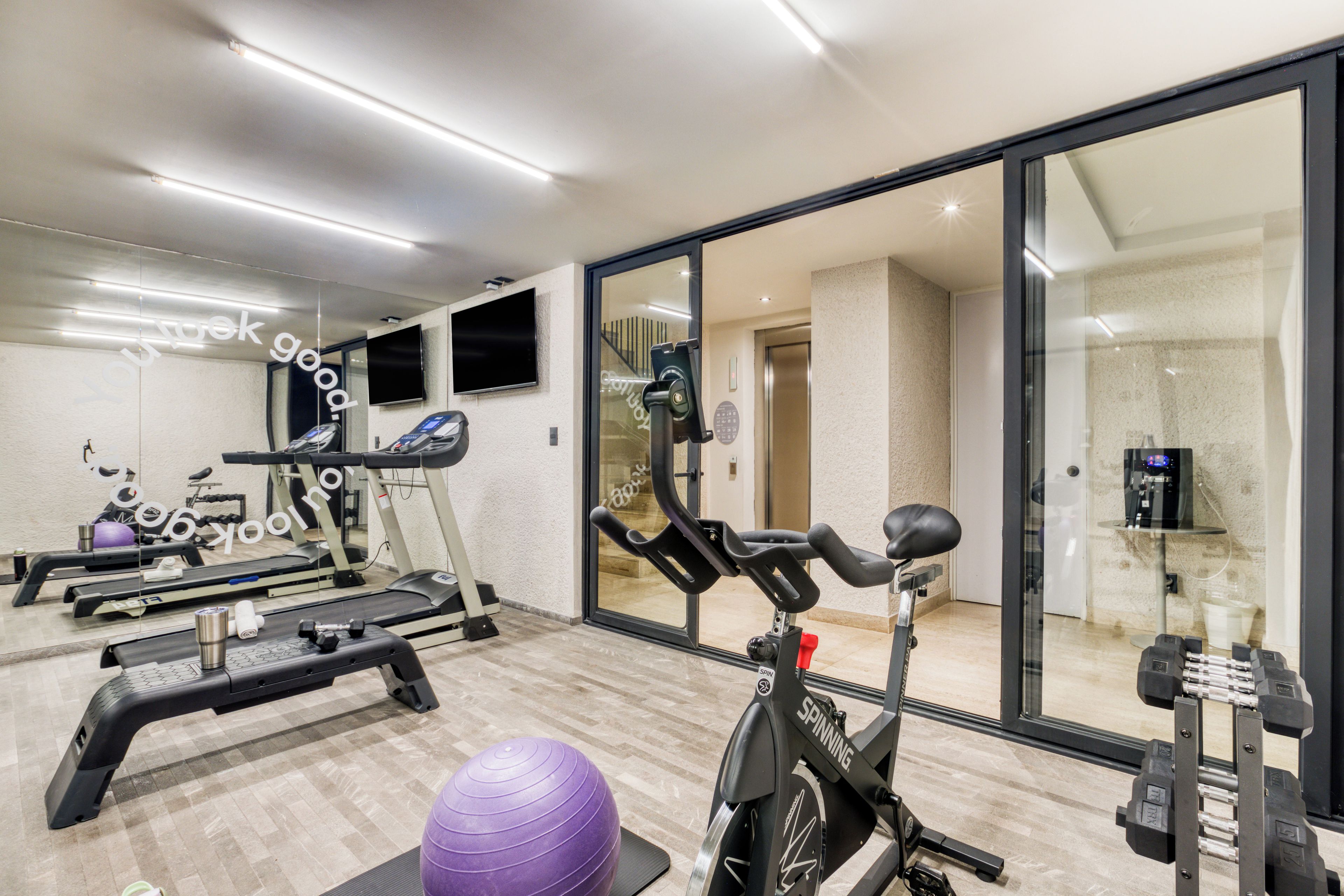 Un gimnasio con equipo de ejercicio, una cinta de correr, una bicicleta estática y un espejo grande.