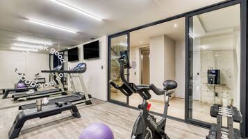 Un gimnasio con equipo de ejercicio, una cinta de correr, una bicicleta estática y un espejo grande.