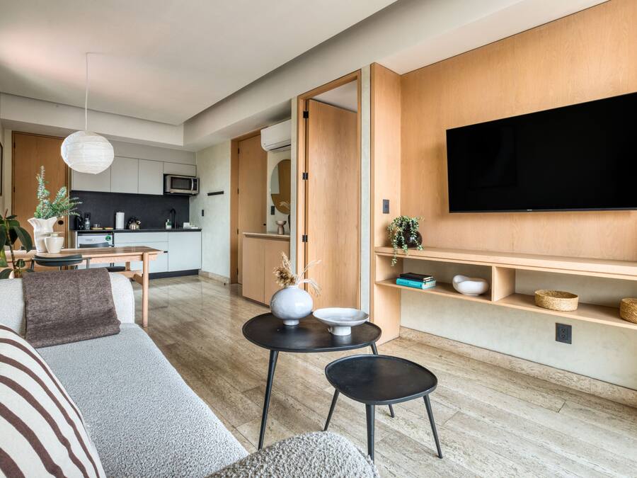 A modern living room with a sofa, a dining table, and a TV mounted on the wall.