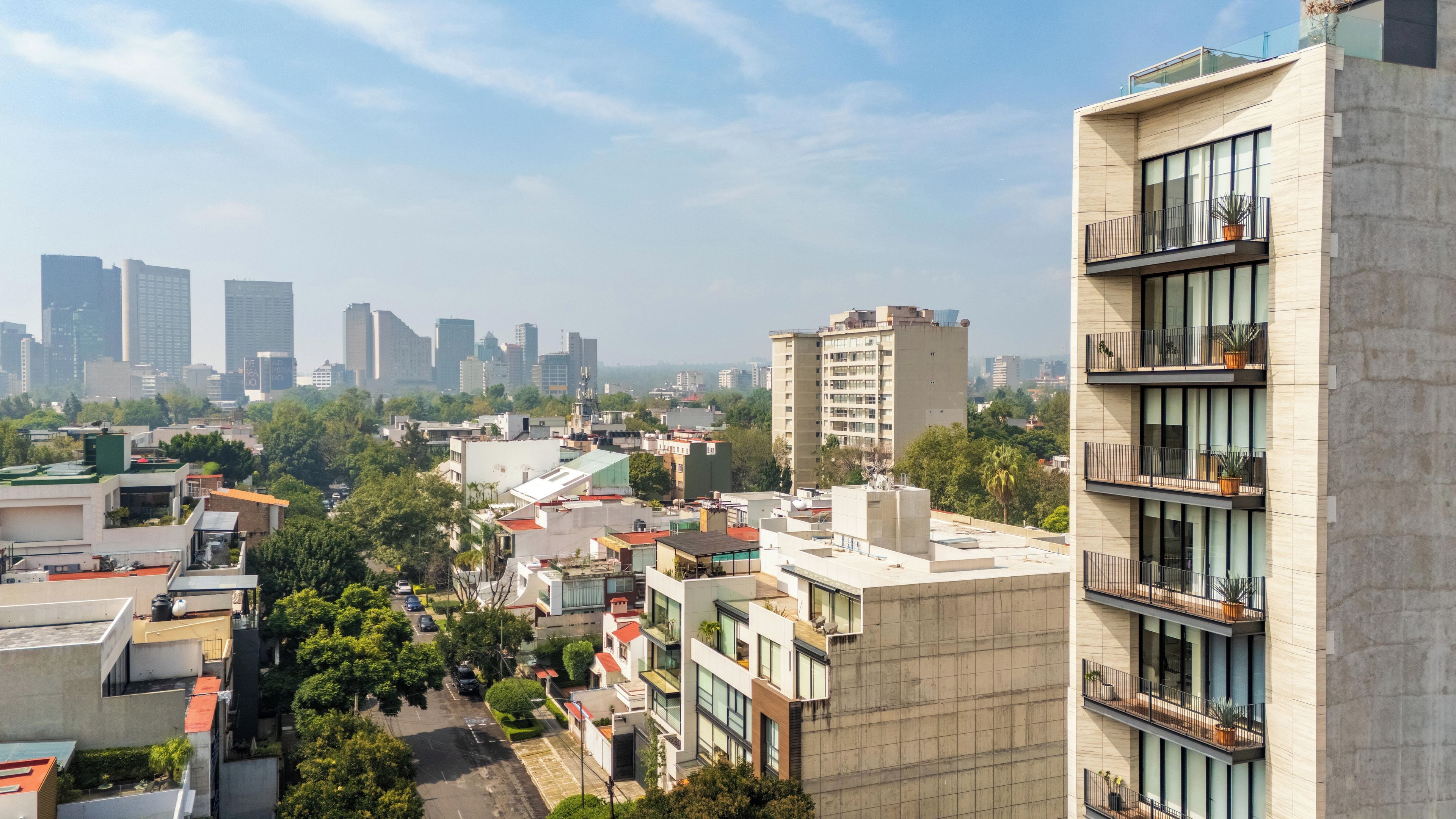 A high-rise building with multiple balconies, a parking area, and a view of a cityscape with various buildings.