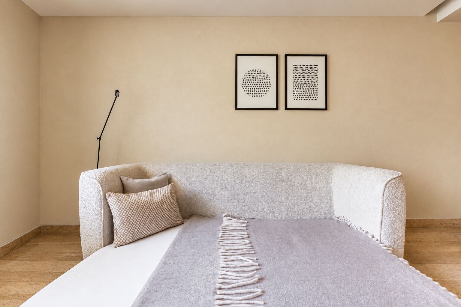 Una habitación minimalista con una cama, un sofá, una lámpara de pie y dos obras de arte enmarcadas en la pared.