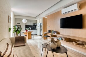 A modern living room with a sofa, coffee table, and TV. There is a kitchen area in the background with a microwave and a dining table. - ULIV Aristo Polanco (Ciudad de México)