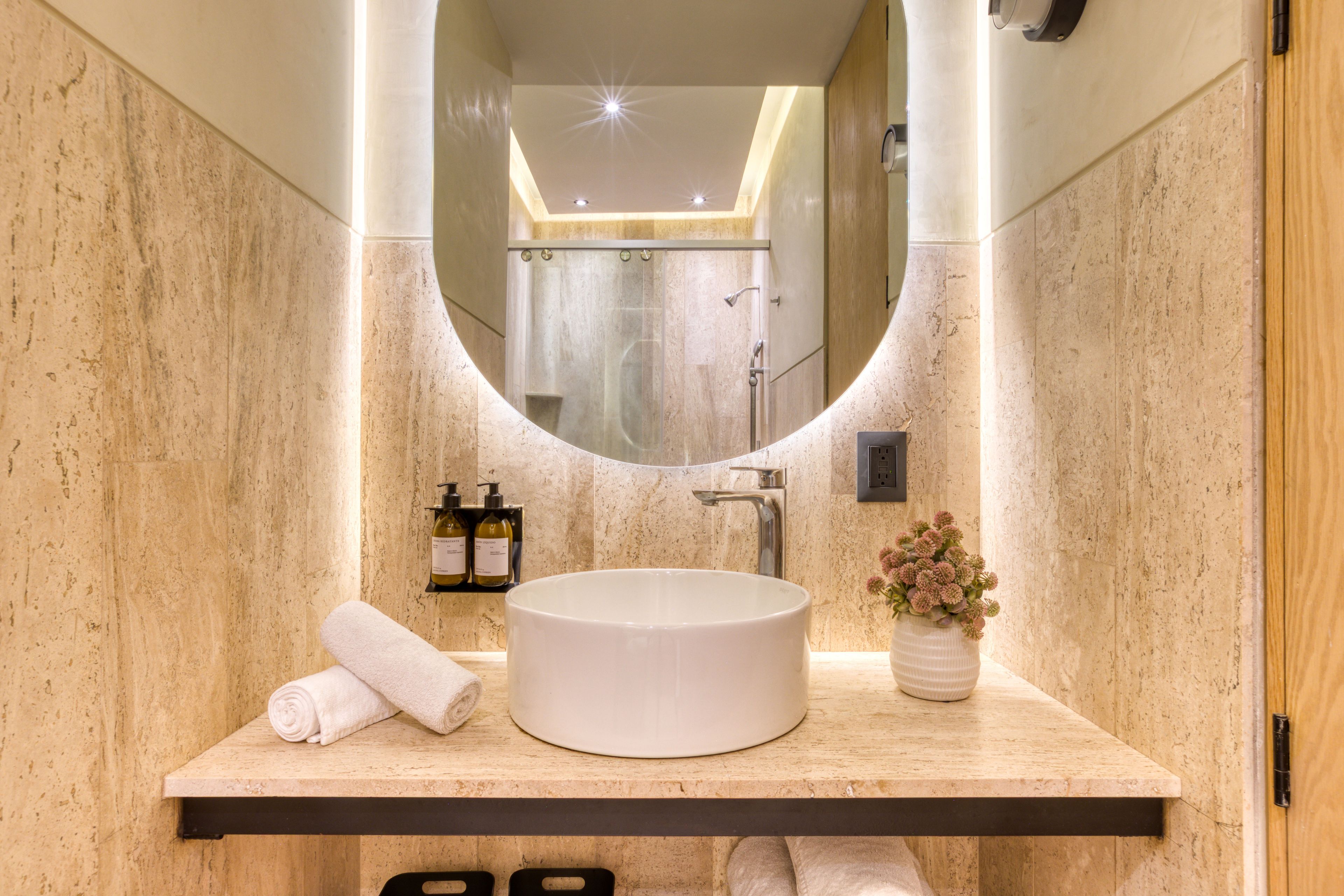 Un baño con un lavabo redondo, un espejo, una toalla y un florero con flores.