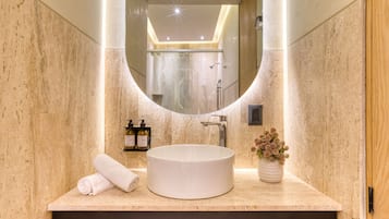 Un baño con un lavabo redondo, un espejo, una toalla y un florero con flores.