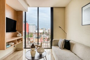 Una sala de estar moderna con un ventanal grande, un televisor de pantalla plana, un sofá y una mesa de centro con adornos.
