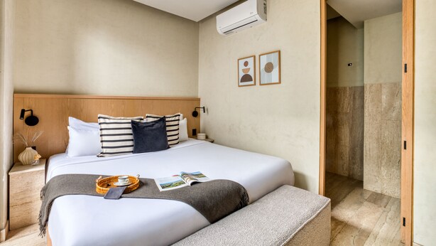 Habitación de hotel con cama, mesitas de noche, aire acondicionado y puerta que da a un baño.
