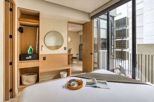 Une chambre d’hôtel comprenant un lit, une table de chevet, un miroir, une fenêtre donnant sur la ville et un balcon.