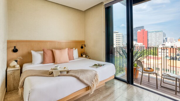 Una habitación de hotel con una cama grande, una mesita de noche, un escritorio, una ventana con vistas a la ciudad y un balcón con una silla y una mesa.