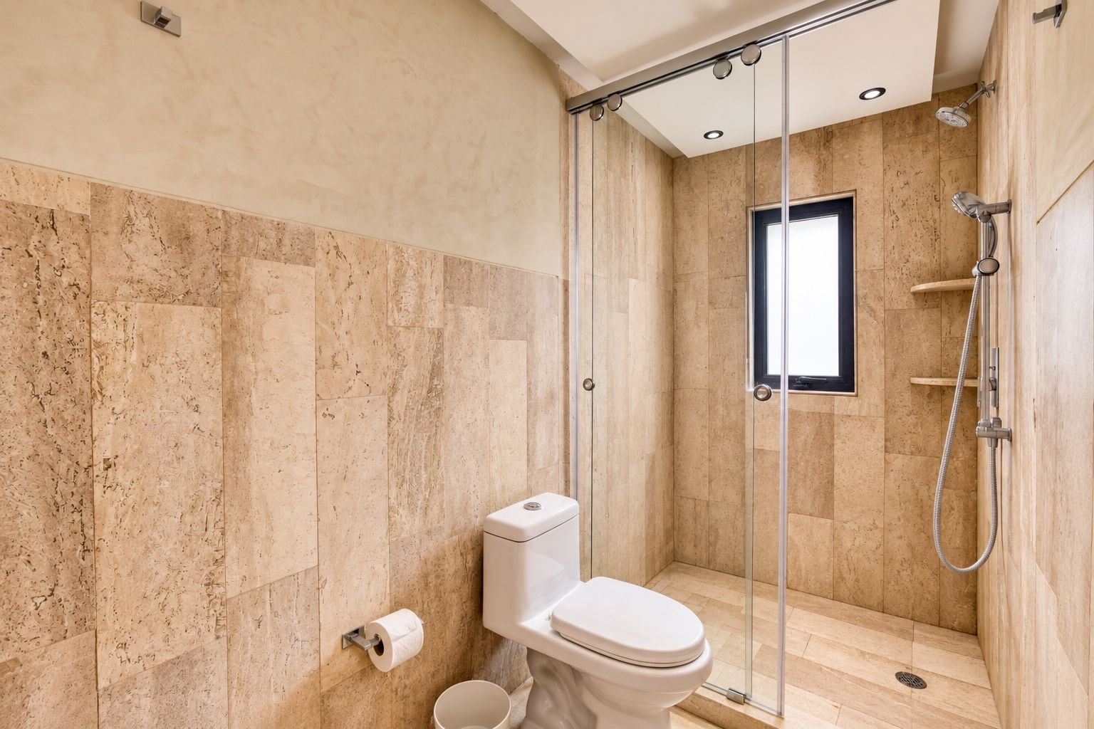 A modern bathroom with a glass-enclosed shower, a toilet, and a marble wall.