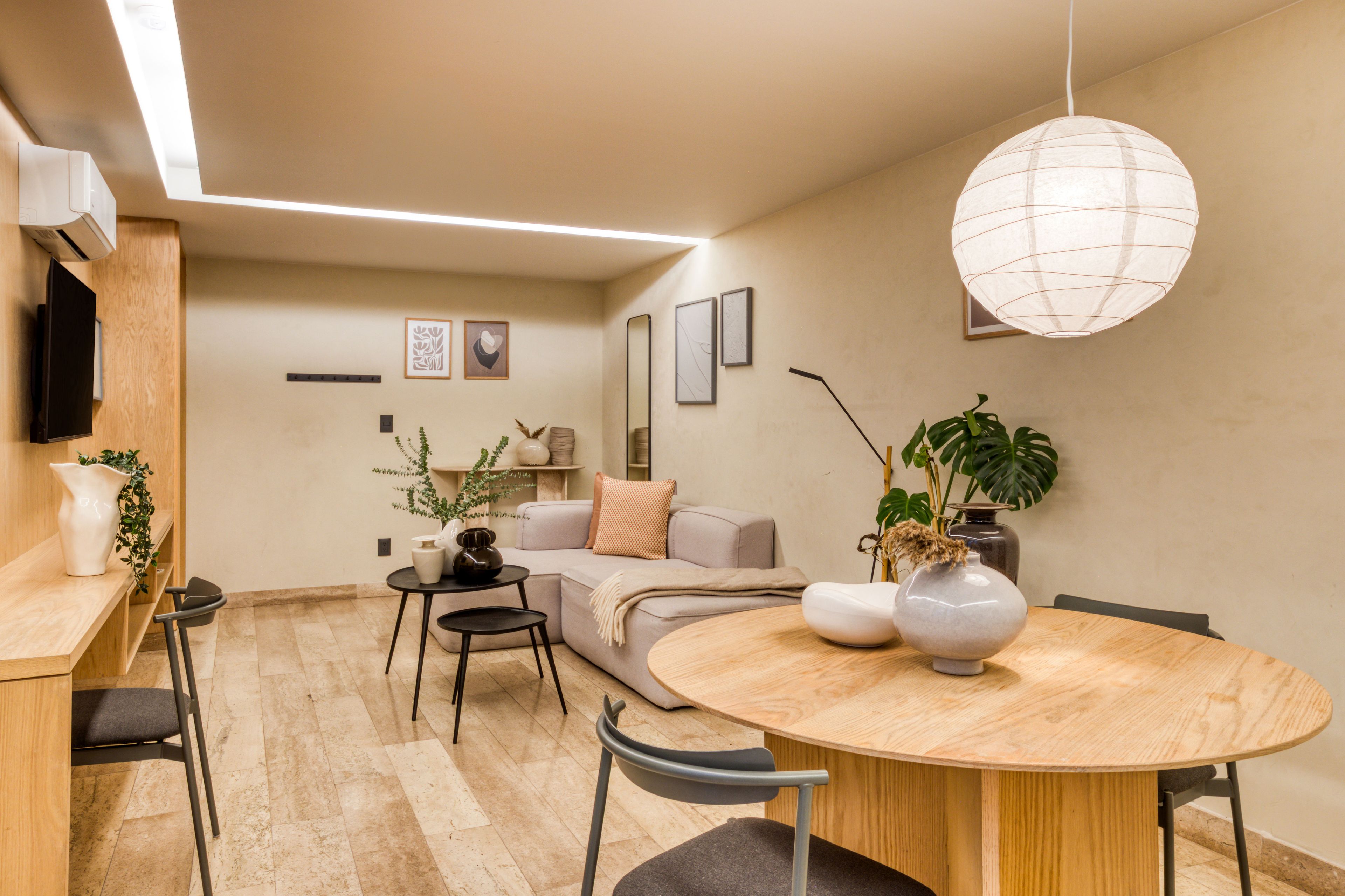 Un salon moderne avec une table à manger ronde en bois, un canapé et un téléviseur fixé au mur.