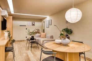 Uma sala de estar moderna com uma mesa de jantar redonda de madeira, um sofá e uma TV na parede.