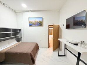 Een slaapkamer met een bed, een bureau, een televisie en een deur naar een andere kamer.