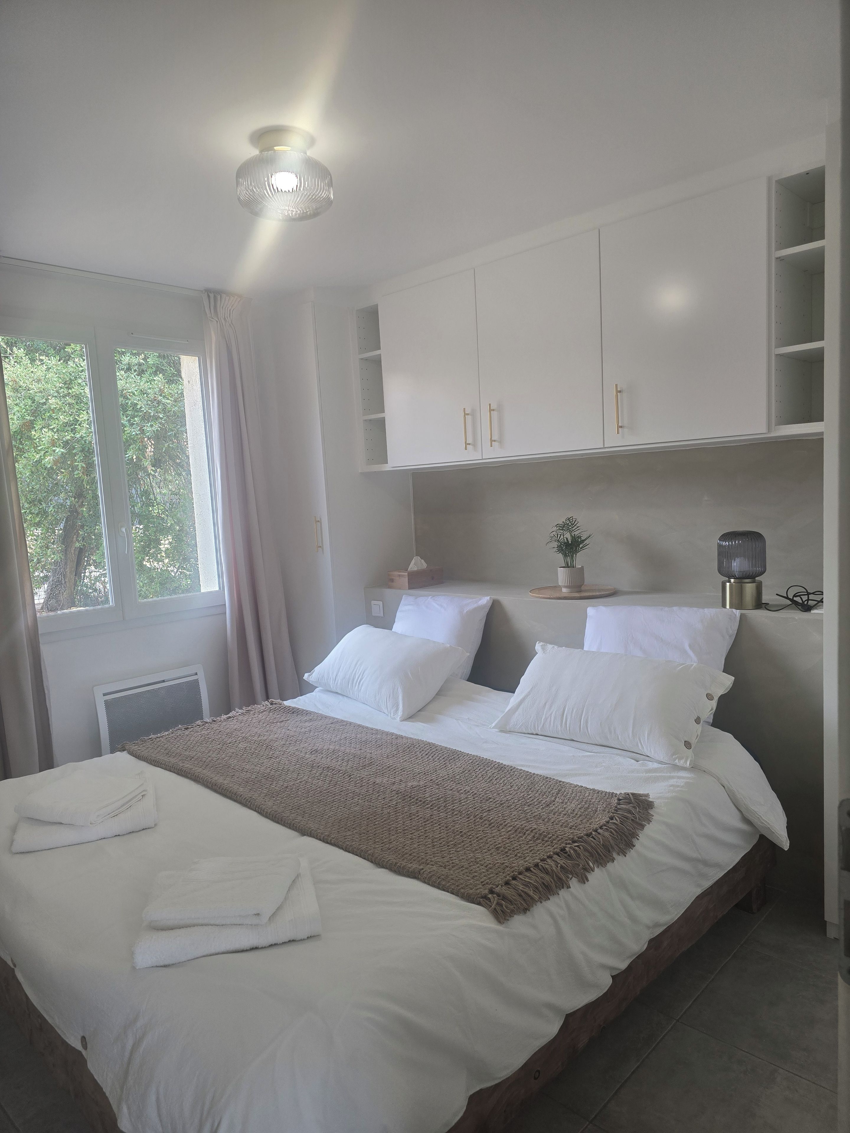 A bedroom with a large bed, white bedding, a ceiling light, and a window with curtains.