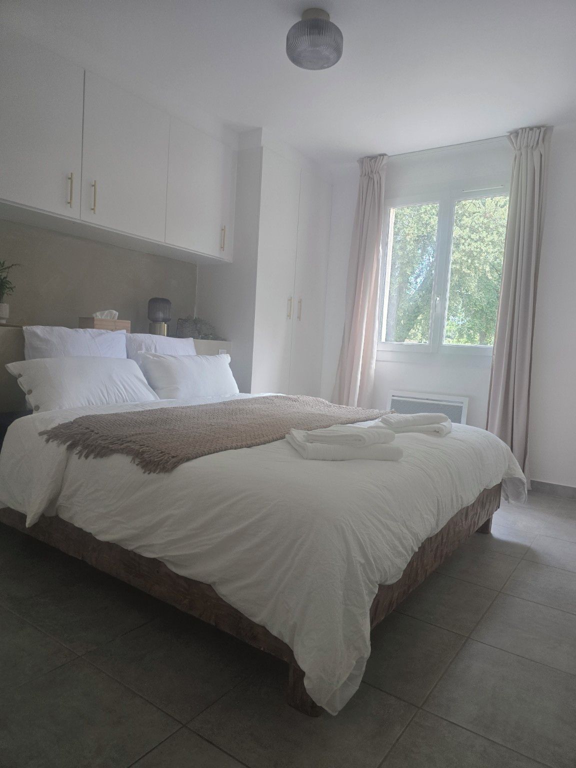 A bedroom with a large bed, a bedside table, a lamp, and a window with curtains.