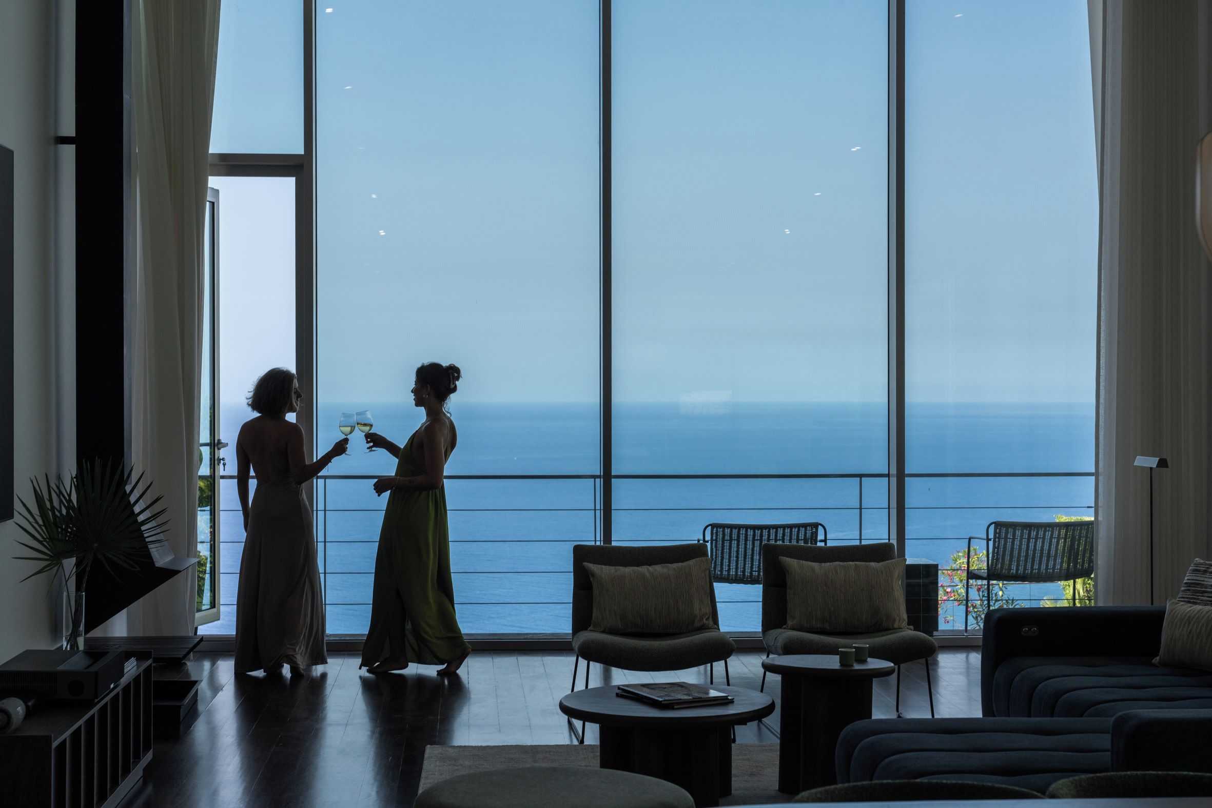Une pièce spacieuse avec de grandes fenêtres donnant sur la mer, aménagée avec un canapé, des fauteuils et une table basse.
