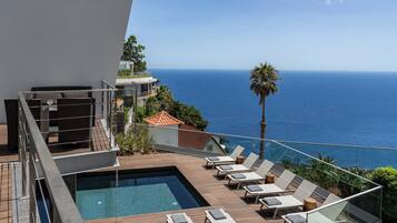 A rooftop pool area with lounge chairs and a view of the ocean.