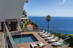 Zona de piscina al terrat amb gandules i vista a l'oceà.