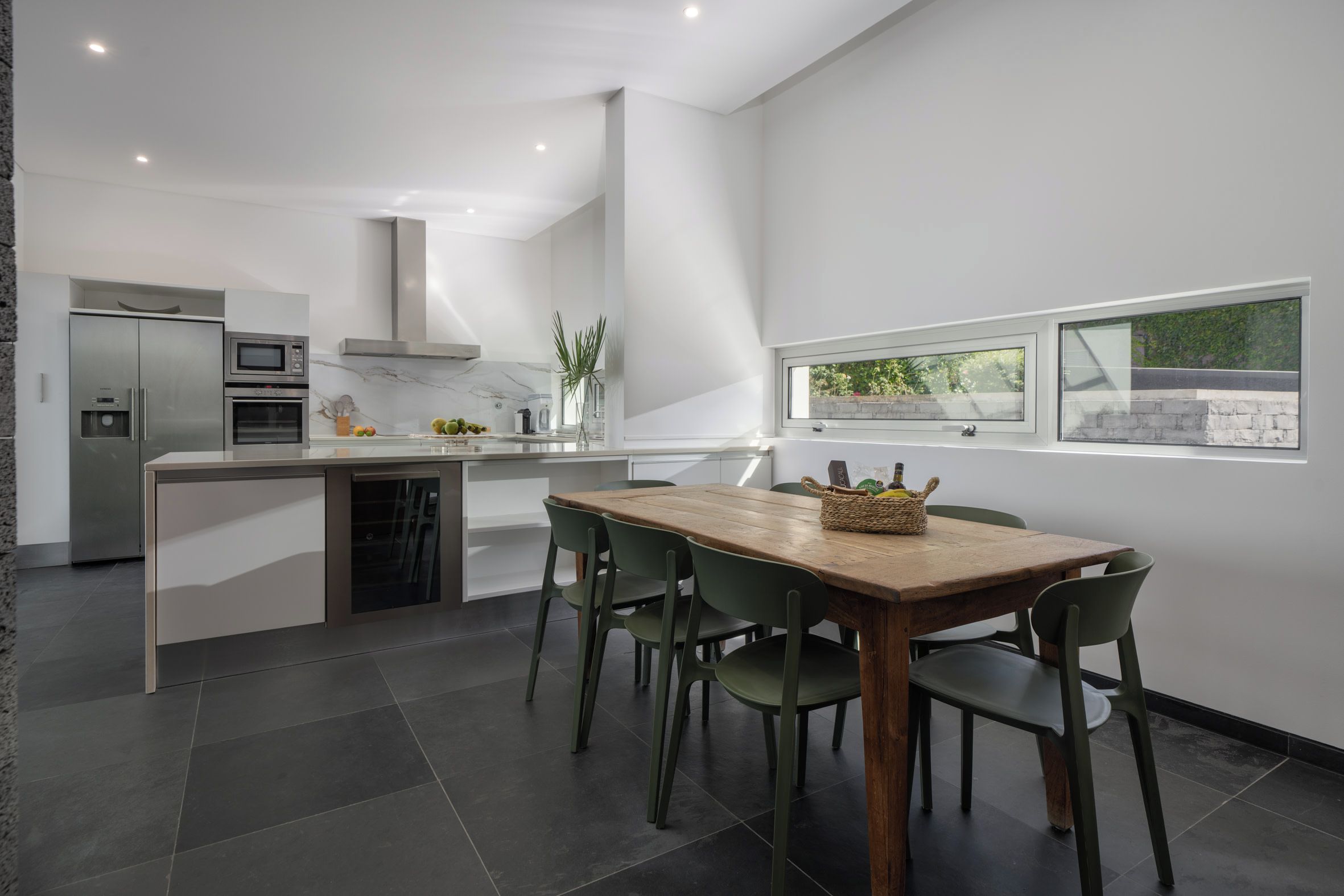 Una cocina moderna con una isla central, electrodomésticos integrados y un comedor con mesa y sillas de madera.