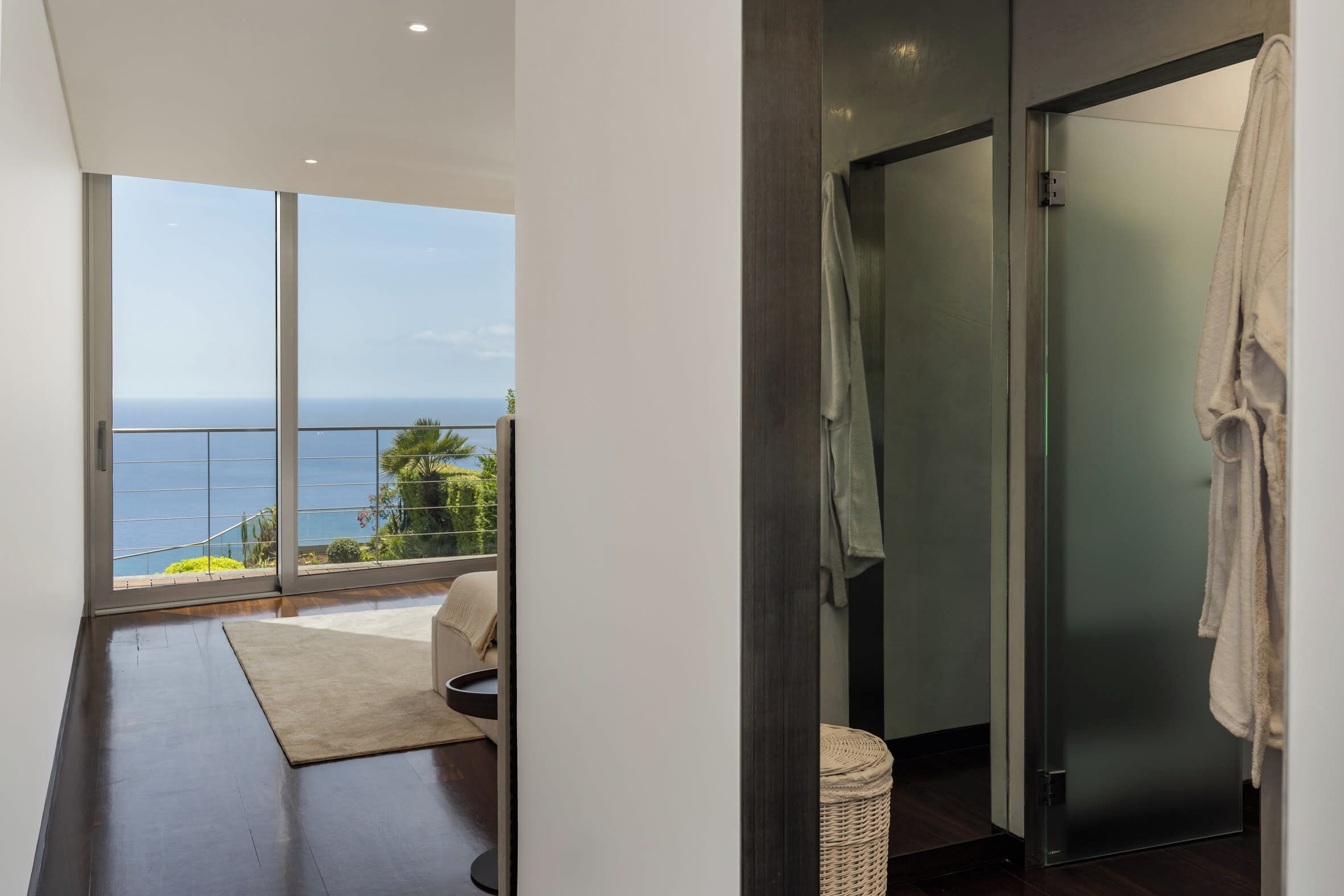 Une salle de bain moderne avec une porte en verre, une serviette accrochée au mur et une vue sur l’océan.