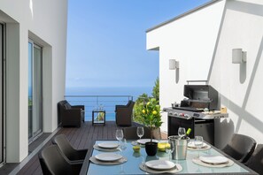 Un balcon avec une table à manger pour deux personnes, un barbecue et une vue sur la mer.