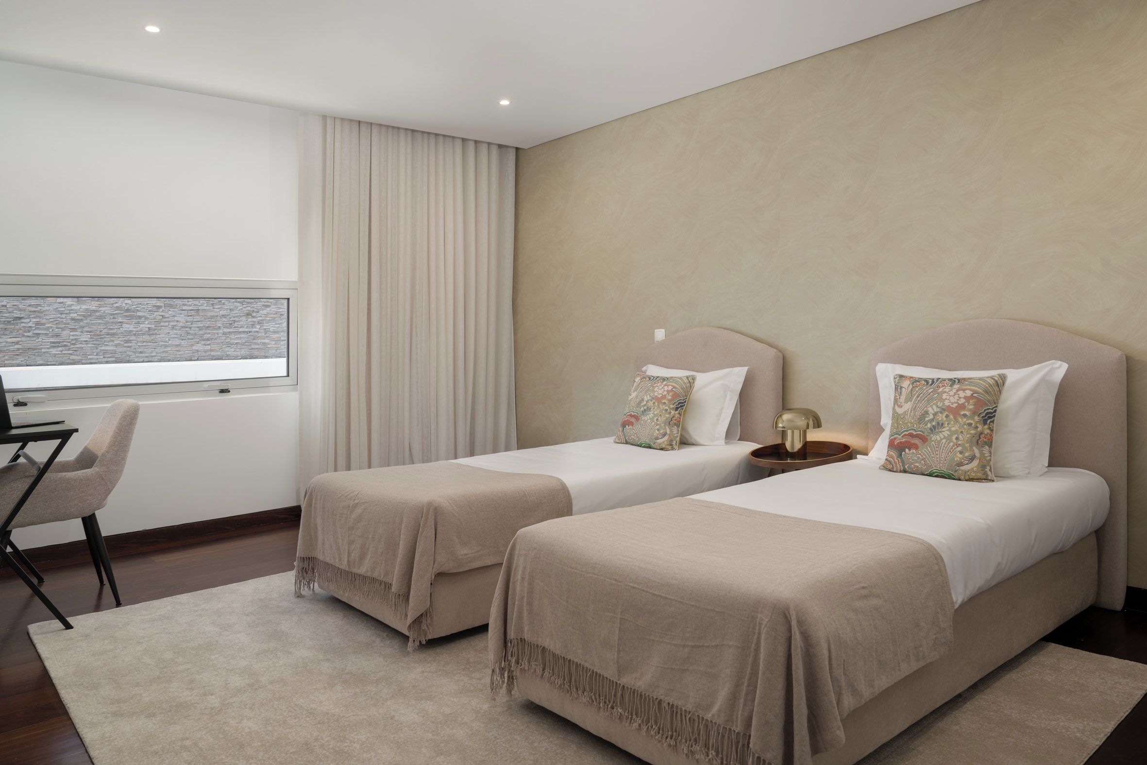 Quarto de hotel com duas camas, uma escrivaninha e uma cadeira.